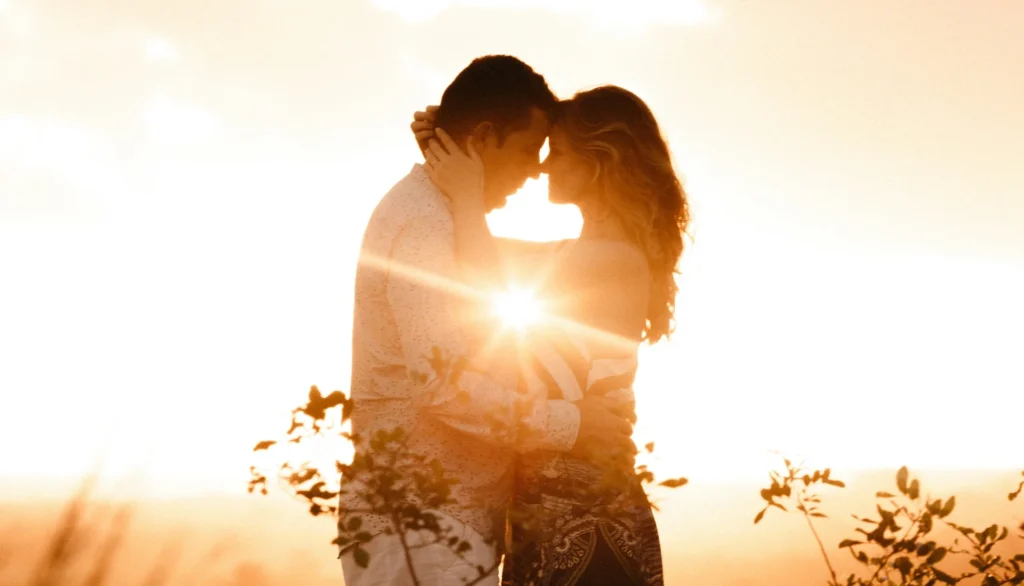a man and woman kissing in front of the sun